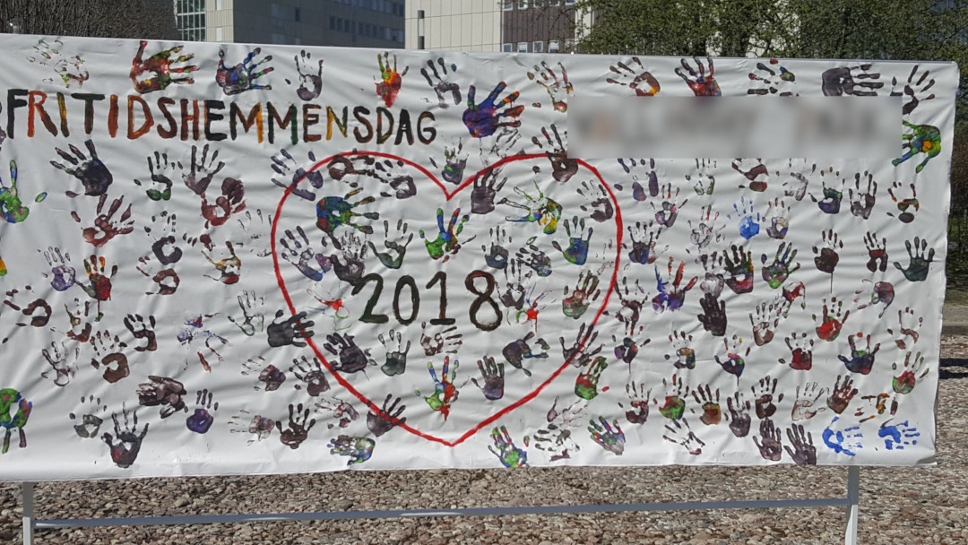 Um mural de mãos feito pelos alunos da escola pra celebrar o fim do semetres.  Várias marcas de mãos feitas com tintas variadas, um coração desenhado no meio e mostrando o ano, 2018.