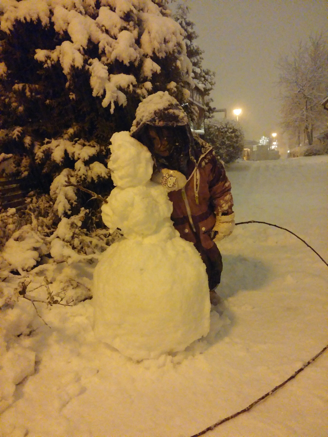 Uma criança numa rua coberta de neve com seu boneco de neve.